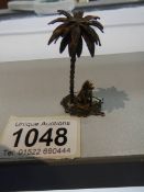 A miniature white metal dog under palm tree (possibly silver but not marked).