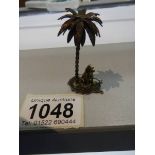 A miniature white metal dog under palm tree (possibly silver but not marked).