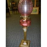 A brass Corinthian column oil lamp with cranberry glass font and shade.