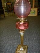 A brass Corinthian column oil lamp with cranberry glass font and shade.