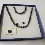 A black pearl necklace, bracelet and earrings.