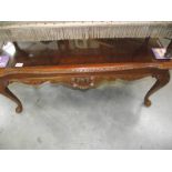 A dark wood stained carved long coffee table with glass top.
