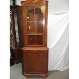 A light wood (yew) corner cabinet.