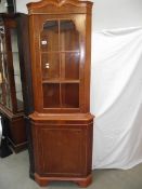 A light wood (yew) corner cabinet.