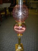 A Brass Corinthian column oil lamp with cranberry cut glass font and shade.