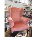 A pink wing arm chair on Queen Anne style legs.