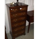 A darkwood stained tall chest of drawers with brass handles