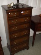 A darkwood stained tall chest of drawers with brass handles