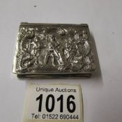 A snuff box in white metal with embossed figures to front.