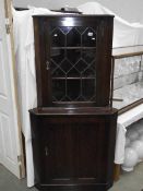 A dark oak corner cupboard with leaded glass door.