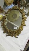 An oval mirror in metal vine leaf frame.