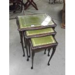 A darkwood stained nest of 3 tables with green/gold leather insets and glass tops.