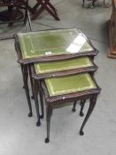 A darkwood stained nest of 3 tables with green/gold leather insets and glass tops.