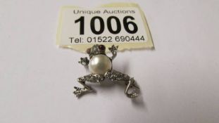 A silver frog brooch with pearl body and ruby eyes.