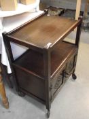 A 1930's dark oak tea trolley with carved cupboard door to base (collect only).