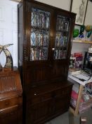 A dark oak leaded book case with cupboard base and carved drop front.