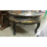 A circular Chinese lacquered coffee table with applied figures under glass top.