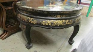 A circular Chinese lacquered coffee table with applied figures under glass top.