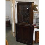 A dark oak corner cupboard with leaded glass door.