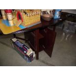 A dark wood stained drop leaf dining table with cupboard in base.