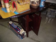 A dark wood stained drop leaf dining table with cupboard in base.