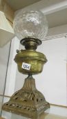 A Victorian oil lamp with brass font on cast iron base with burner and shade but missing chimney.