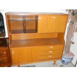 A teak glazed sliding door cabinet with drop down side and three drawers.