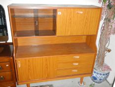 A teak glazed sliding door cabinet with drop down side and three drawers.