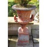Pair of red stone garden urns on plinth.