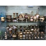 TWO SHELVES OF BRASS ENGRAVED GOBLETS, BRASS AND ENAMEL TEAPOTS BELLS, JARS AND COVERS,