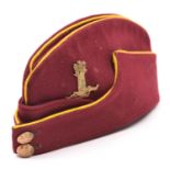 An OR’s crimson field cap of the 11th Hussars, with yellow piping, regimental GM cap badge and GS
