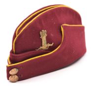 An OR’s crimson field cap of the 11th Hussars, with yellow piping, regimental GM cap badge and GS