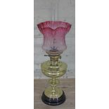 A brass oil lamp with etched cranberry glass shade, height 67cm.