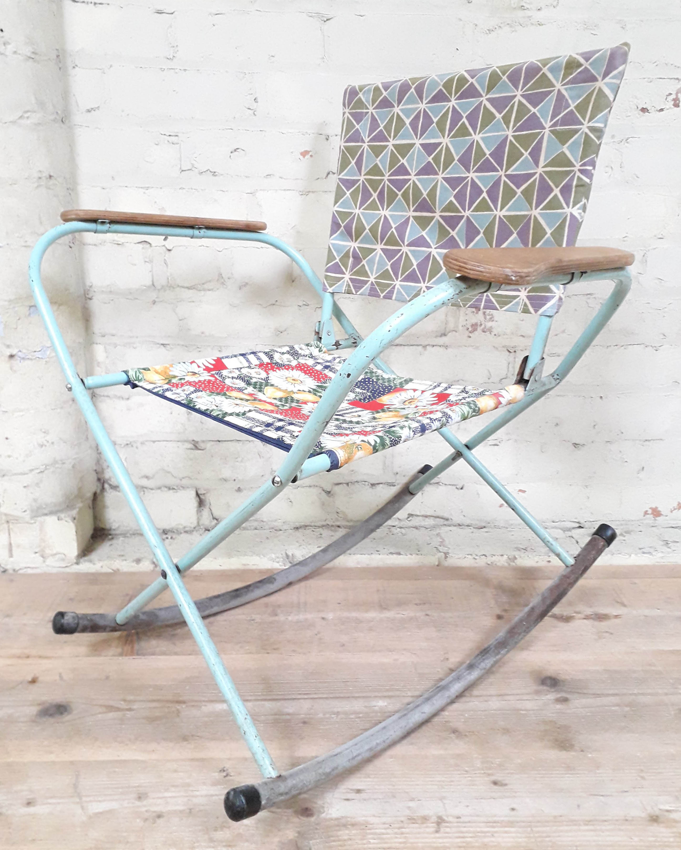 A vintage folding metal rocking chair with plywood armrests.