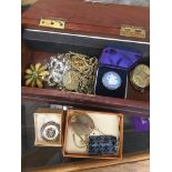 A wooden box of costume jewellery including badges, brooches, a silver mounted Wedgwood cameo brooch