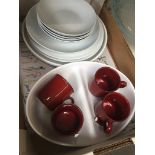 A box of white tableware and some red mugs