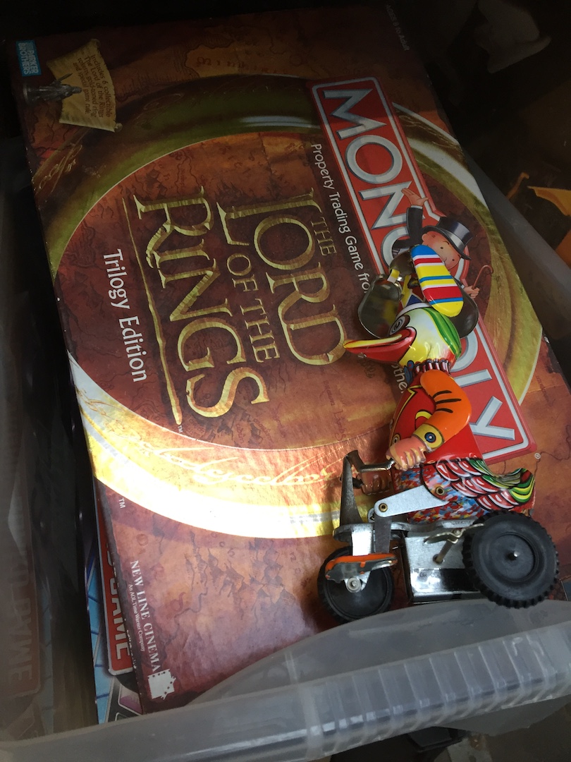 A box of boxed games including Lord of the Rings and a tin plate toy.