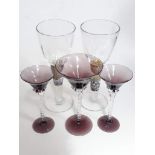 A pair of hand made wine glasses and three purple glasses.