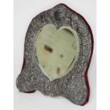 A late Victorian/Edwardian silver framed mirror, the heart shaped bevelled mirror within an embossed