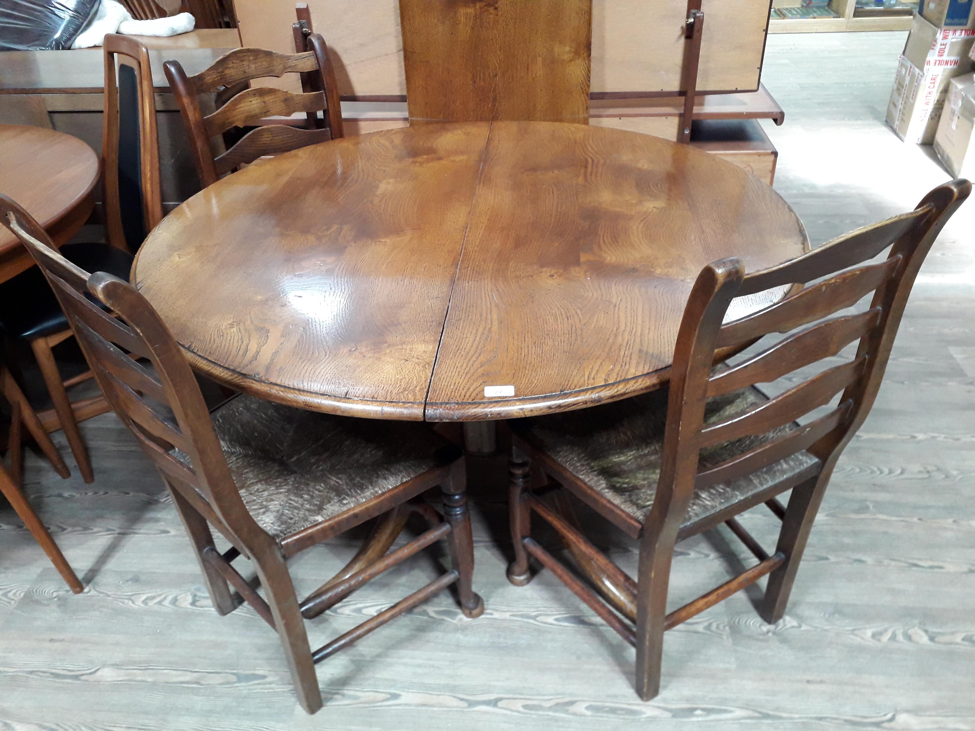 A reproduction oak extending pedestal dining table with single leaf and four ladder back and rush