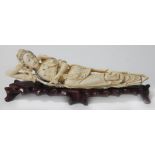 An oriental carved ivory figure depicting a reclining lady on carved wooden stand,