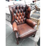 A brown leather chesterfield winged back armchair.