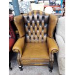 A tan leather chesterfield wing back armchair