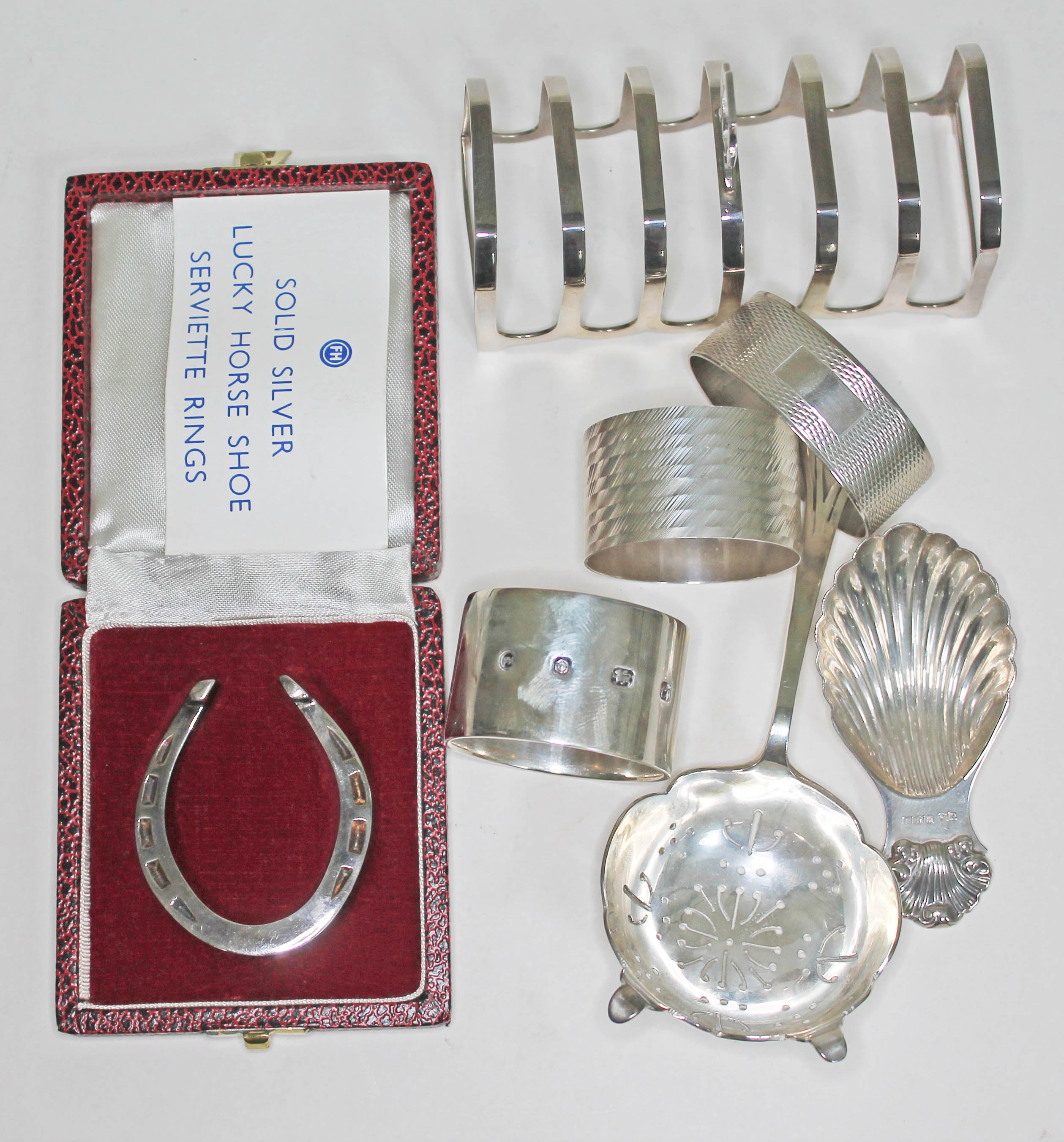 A mixed lot of hallmarked silver comprising three serviette rings, a tea strainer, a Georgian