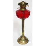 A brass oil lamp with red glass fuel chamber - no shade nor flue glass. Height approx 20 inches.