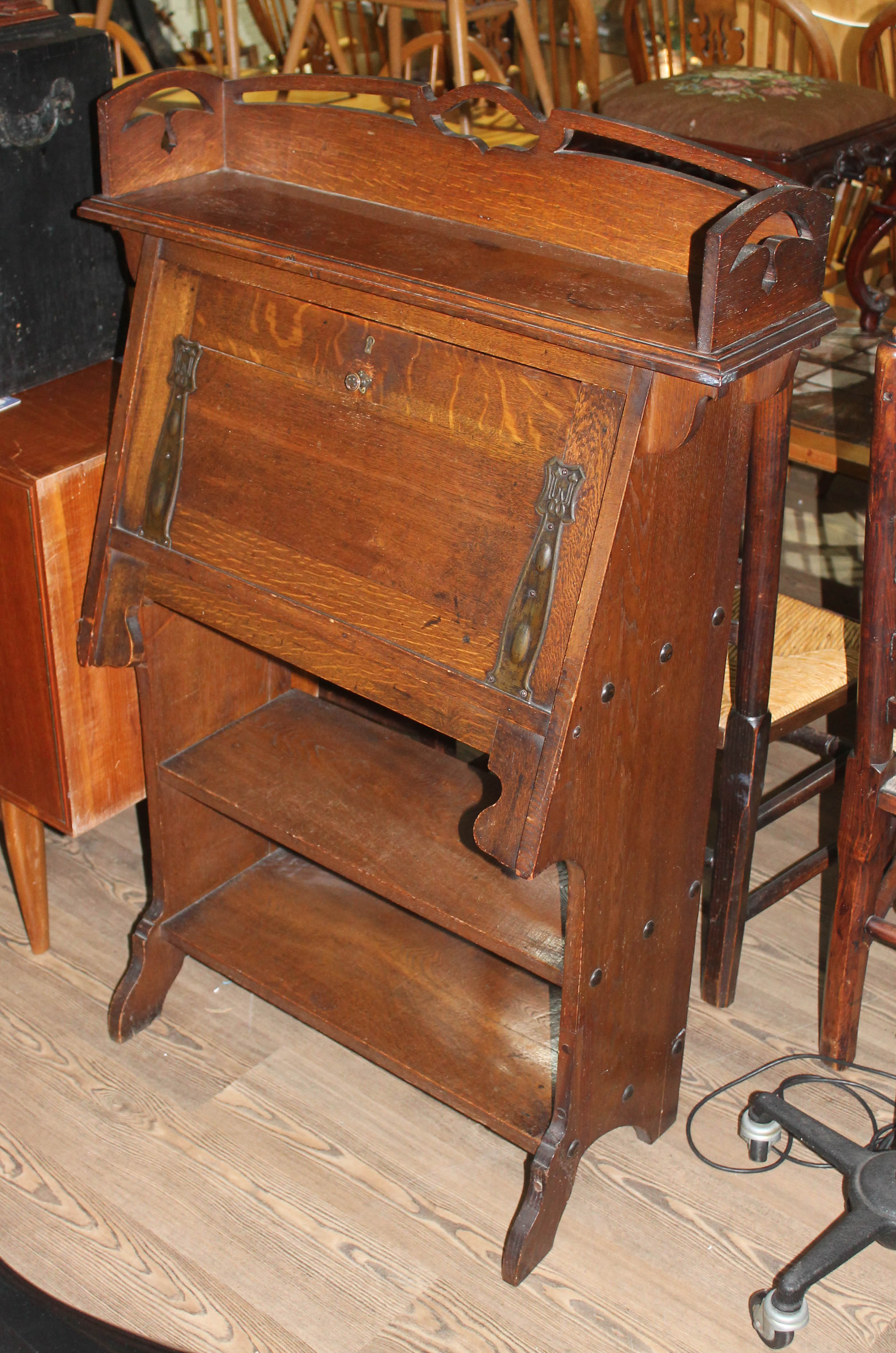 An Arts & Crafts style oak bureau, rail with cut outs and drop down front with straps, in the manner