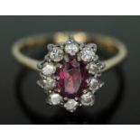 A cluster ring set with a central oval cut pinkish purple almandine garnet and surrounded by ten