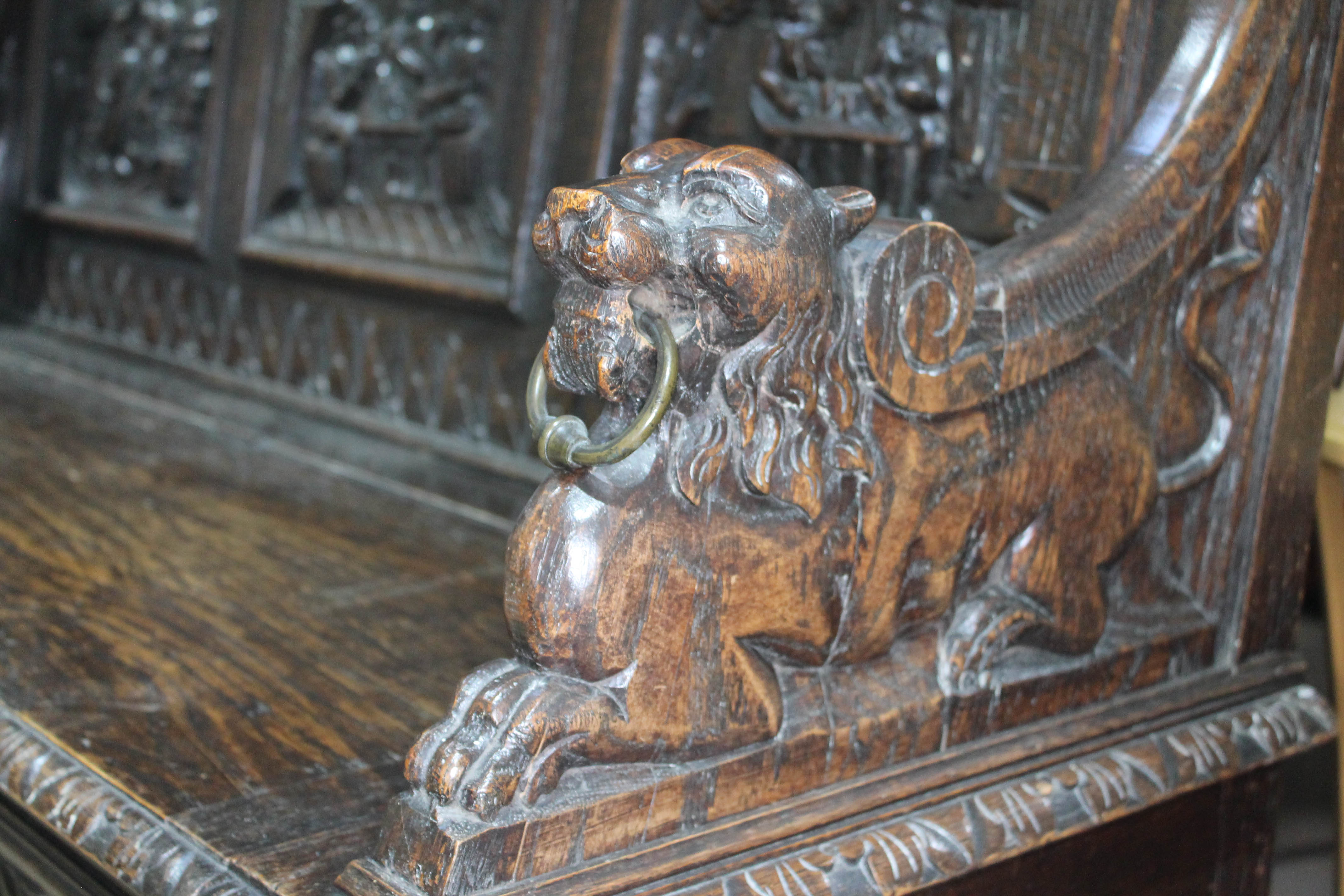 A 19th century carved oak settle with lion arms, carved continental scene panels to back, lift top - Image 4 of 4