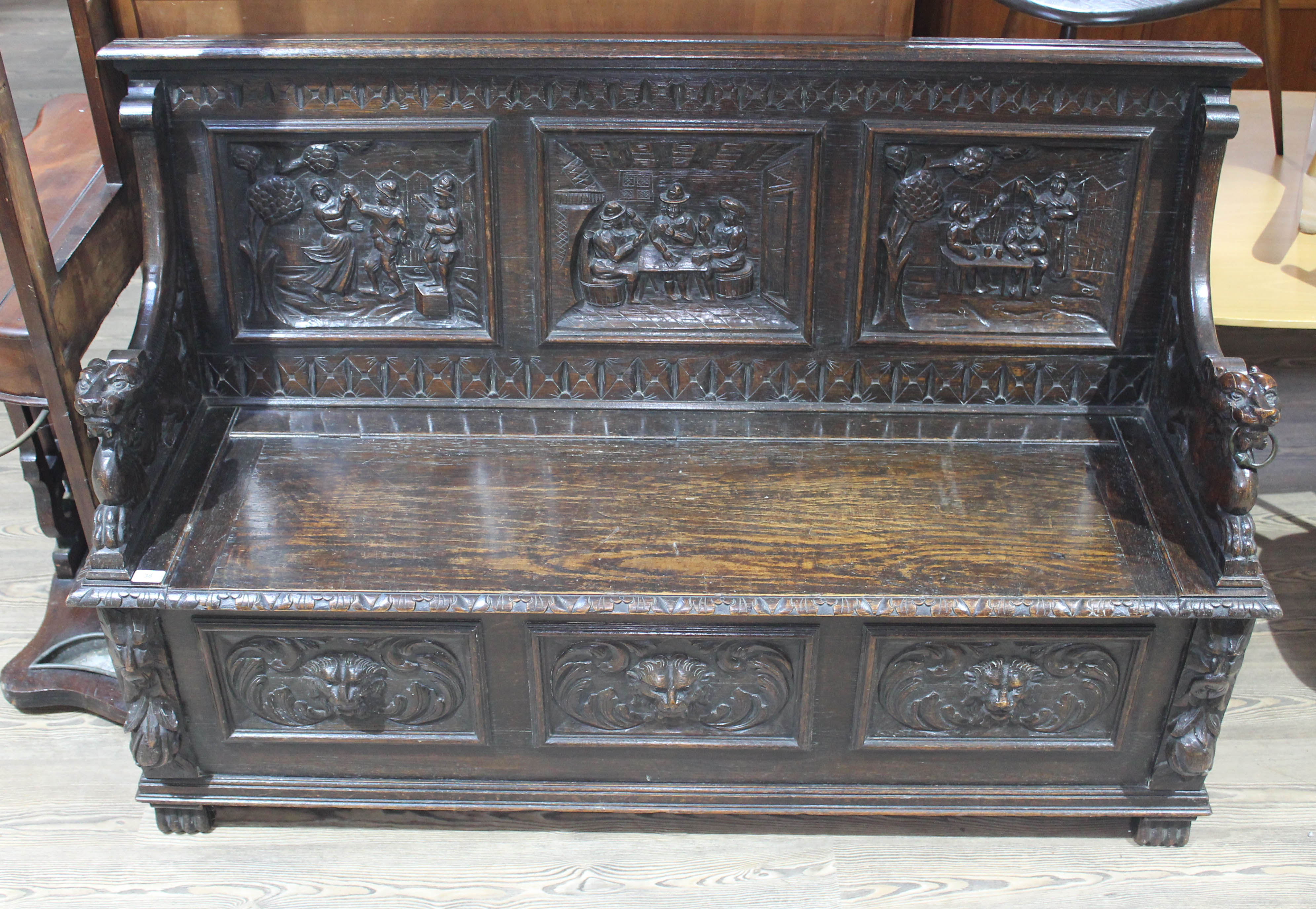 A 19th century carved oak settle with lion arms, carved continental scene panels to back, lift top