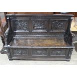 A 19th century carved oak settle with lion arms, carved continental scene panels to back, lift top